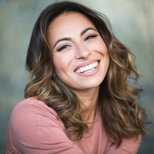 mature woman in blush pink shirt smiling with perfect teeth