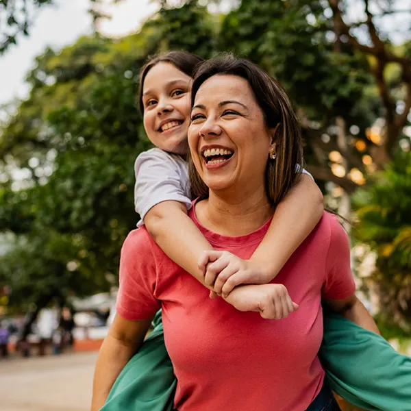 daughter riding on her mom's back outdoors, both smiling and laughing